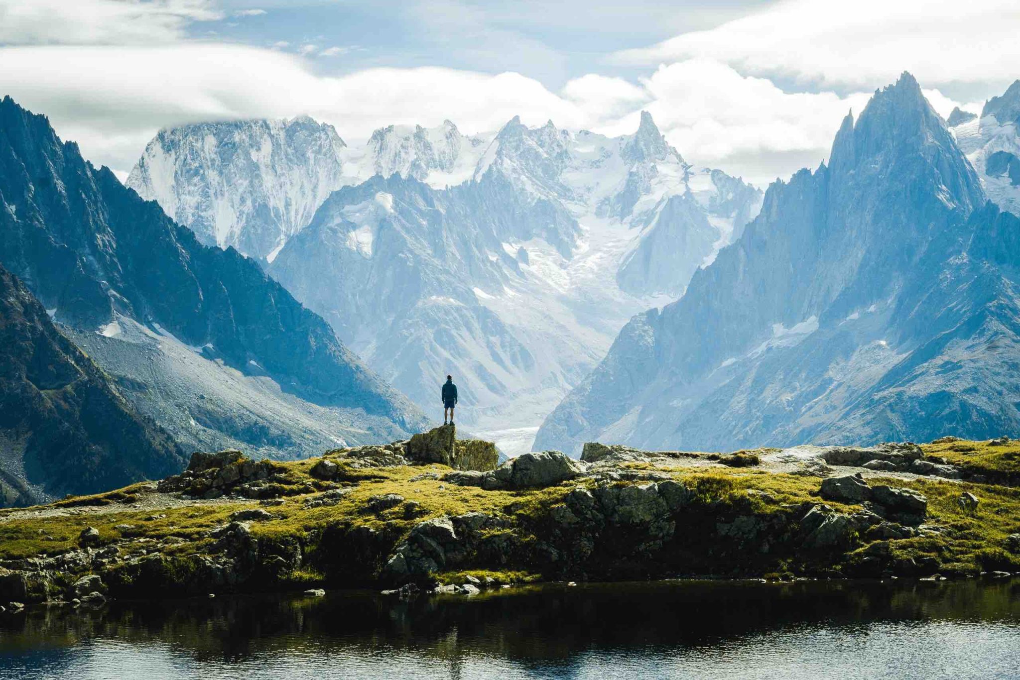 A lone hiker standing on a rocky outcrop overlooking a vast mountain range, a glacial lake in the foreground